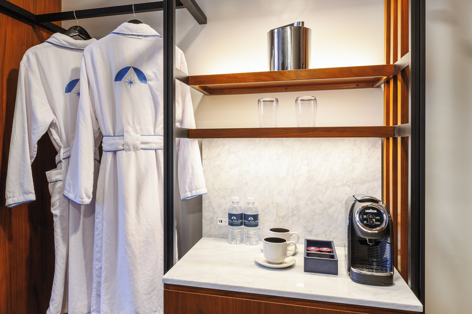 A hotel room with a minibar, a coffee maker, and two bottles of water on the counter.