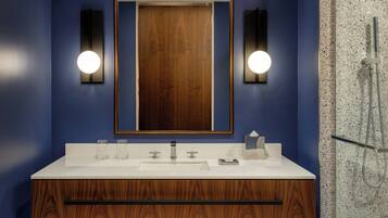 Un baño moderno con tocador de madera, dos luces empotradas en la pared, un espejo grande y zona de ducha.