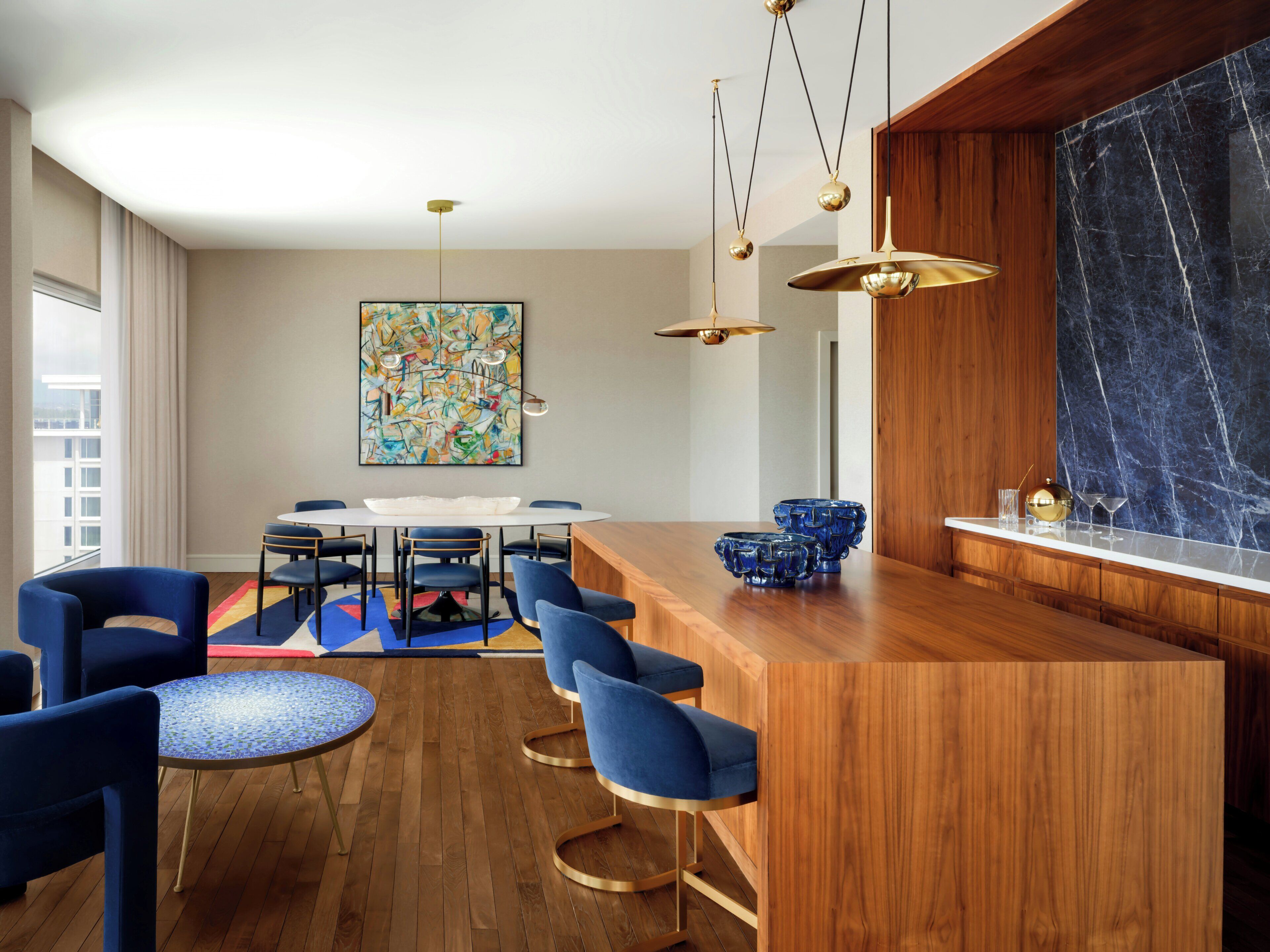 Una cocina moderna con una isla de madera, sillas azules, una mesa redonda y un cuadro abstracto grande en la pared.