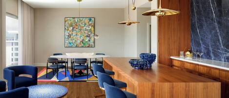 Una cocina moderna con una isla de madera, sillas azules, una mesa redonda y un cuadro abstracto grande en la pared.