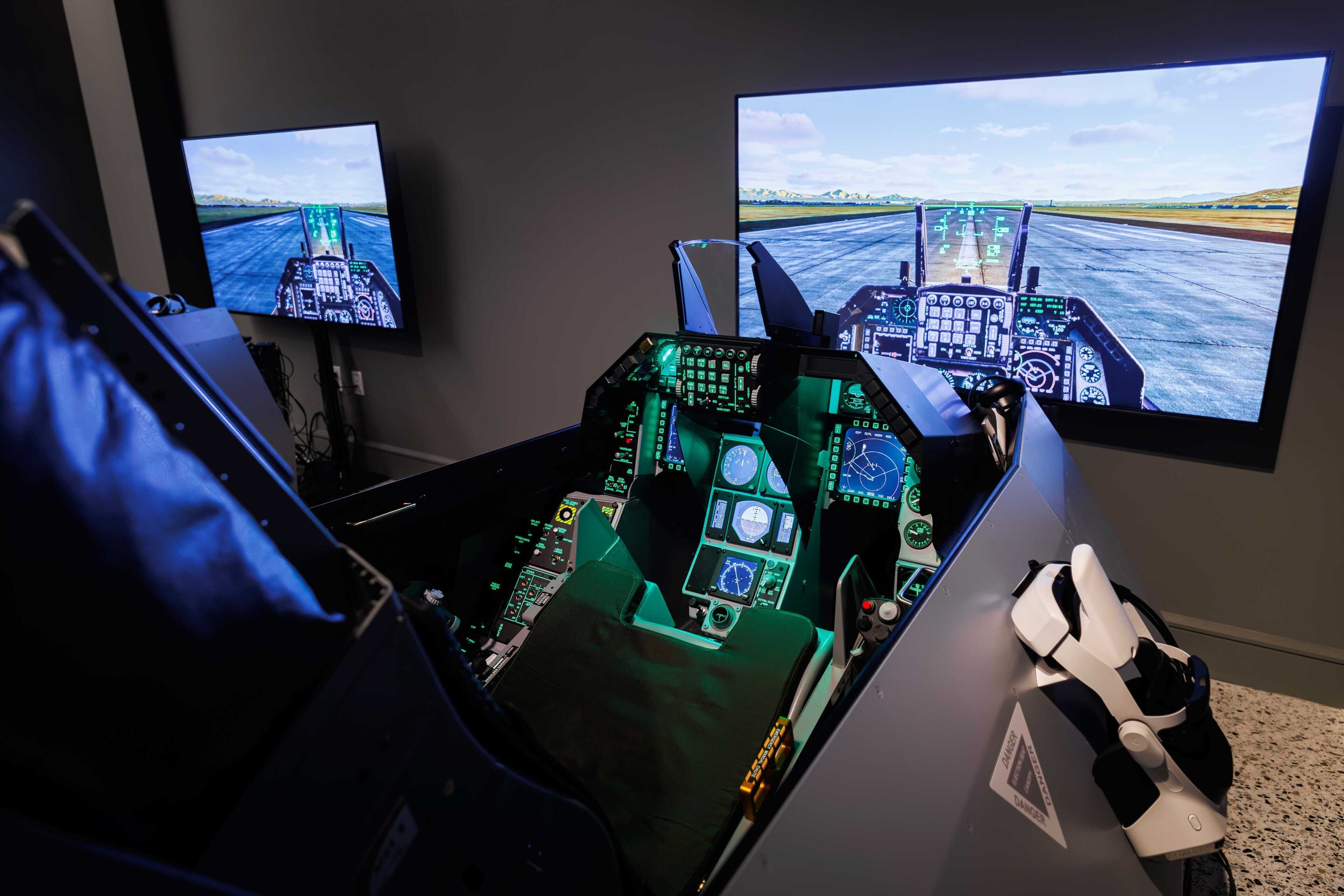 Een vluchtensimulatorcockpit met twee schermen waarop een landingsbaan en een beeld van een vliegtuig te zien is.