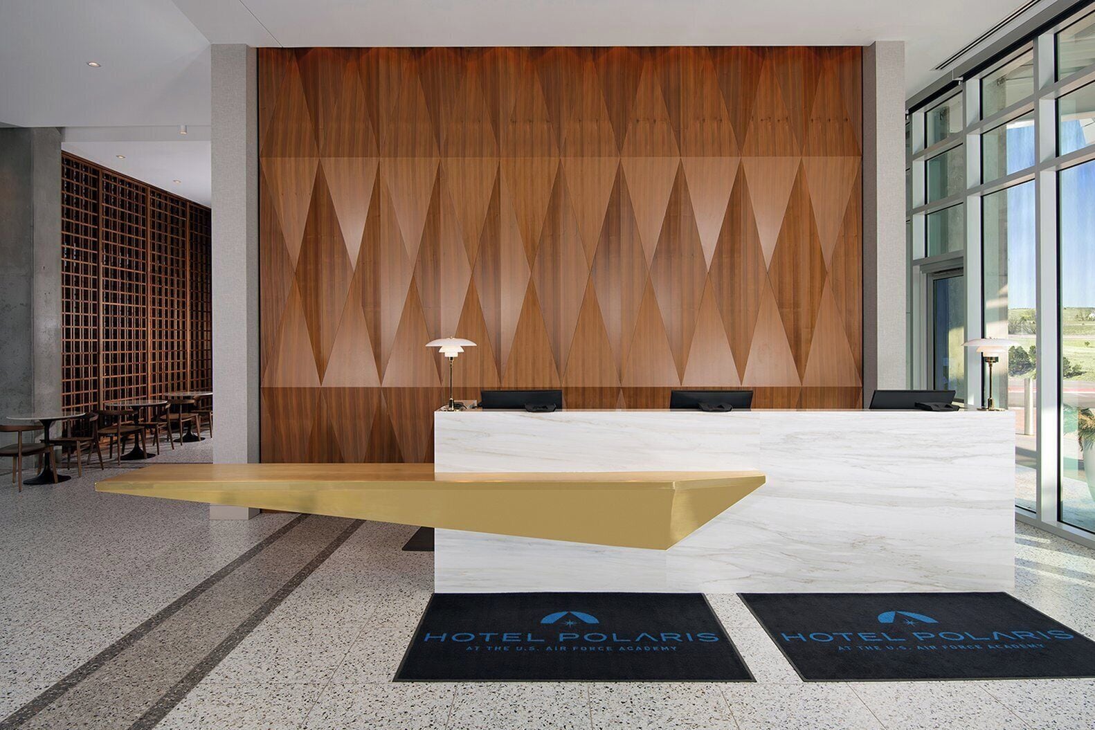 Un mostrador de recepción de hotel con diseño moderno, una pared decorativa de madera y vistas al exterior a través de amplias ventanas.