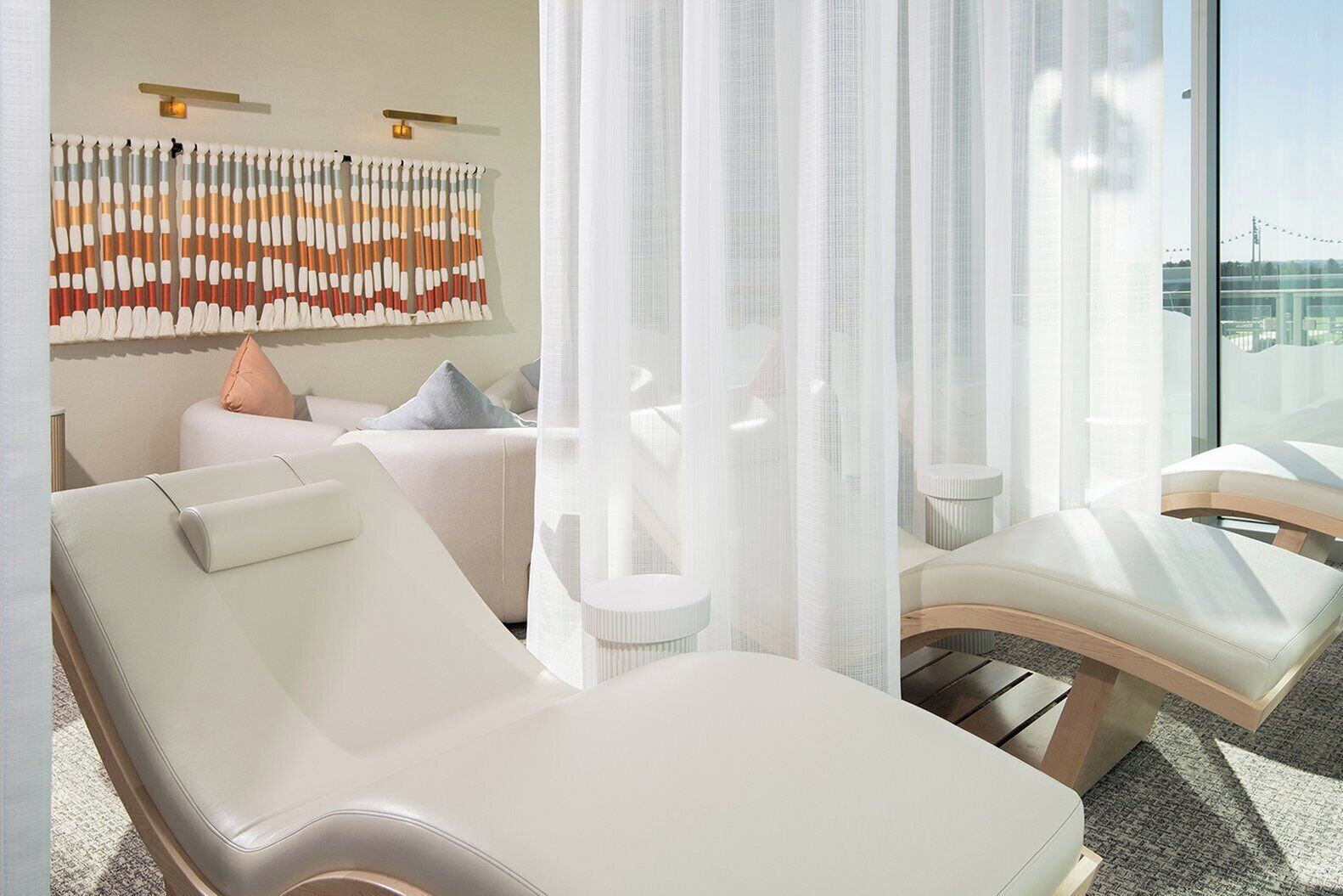 A modern hotel room with a large window, a ceiling-mounted light fixture, and a decorative wall piece.
