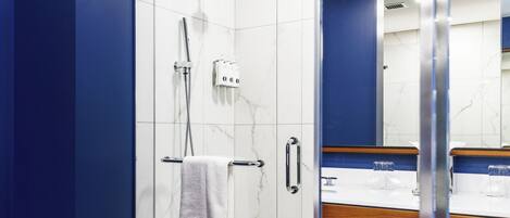Un bagno moderno con box doccia in vetro, un asciugamano bianco su un portasci e un mobile bagno in legno con specchio.