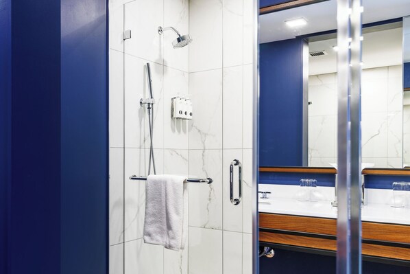 A modern bathroom with a glass shower enclosure, a white towel hanging on a rack, and a wooden vanity with a mirror. - Hotel Polaris (Colorado Springs)