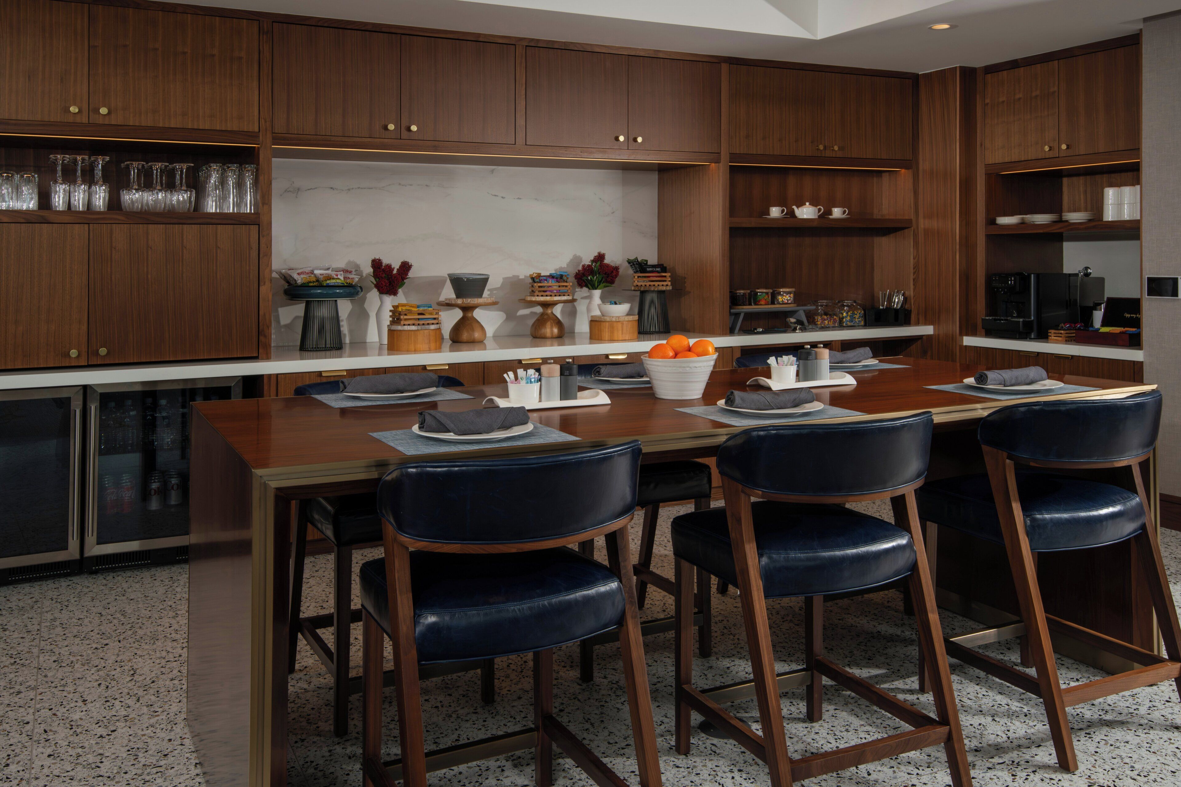 A modern kitchen with wooden cabinets, a marble countertop, and a dining area with a wooden table and black chairs.