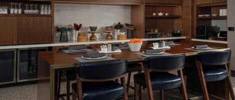 A modern kitchen with wooden cabinets, a marble countertop, and a dining area with a wooden table and black chairs.