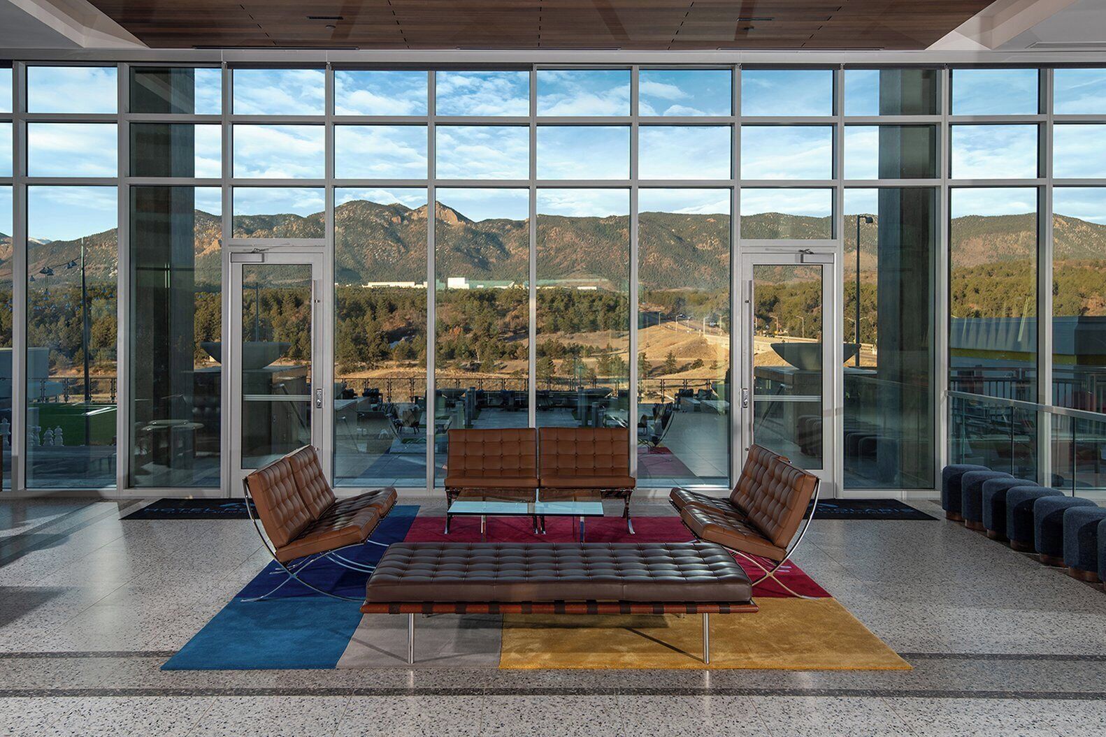 A spacious indoor area with large windows offering a view of mountains and a parking lot. There are two leather sofas and a small table in the center.