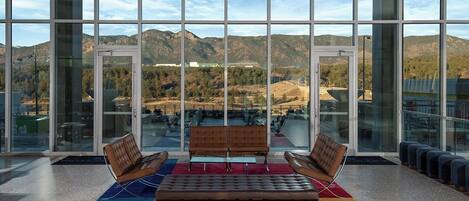 A spacious indoor area with large windows offering a view of mountains and a parking lot. There are two leather sofas and a small table in the center.