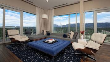 Una sala de estar moderna con un sofá grande, dos sillones, un otomano azul y vistas a montañas a través de amplios ventanales.