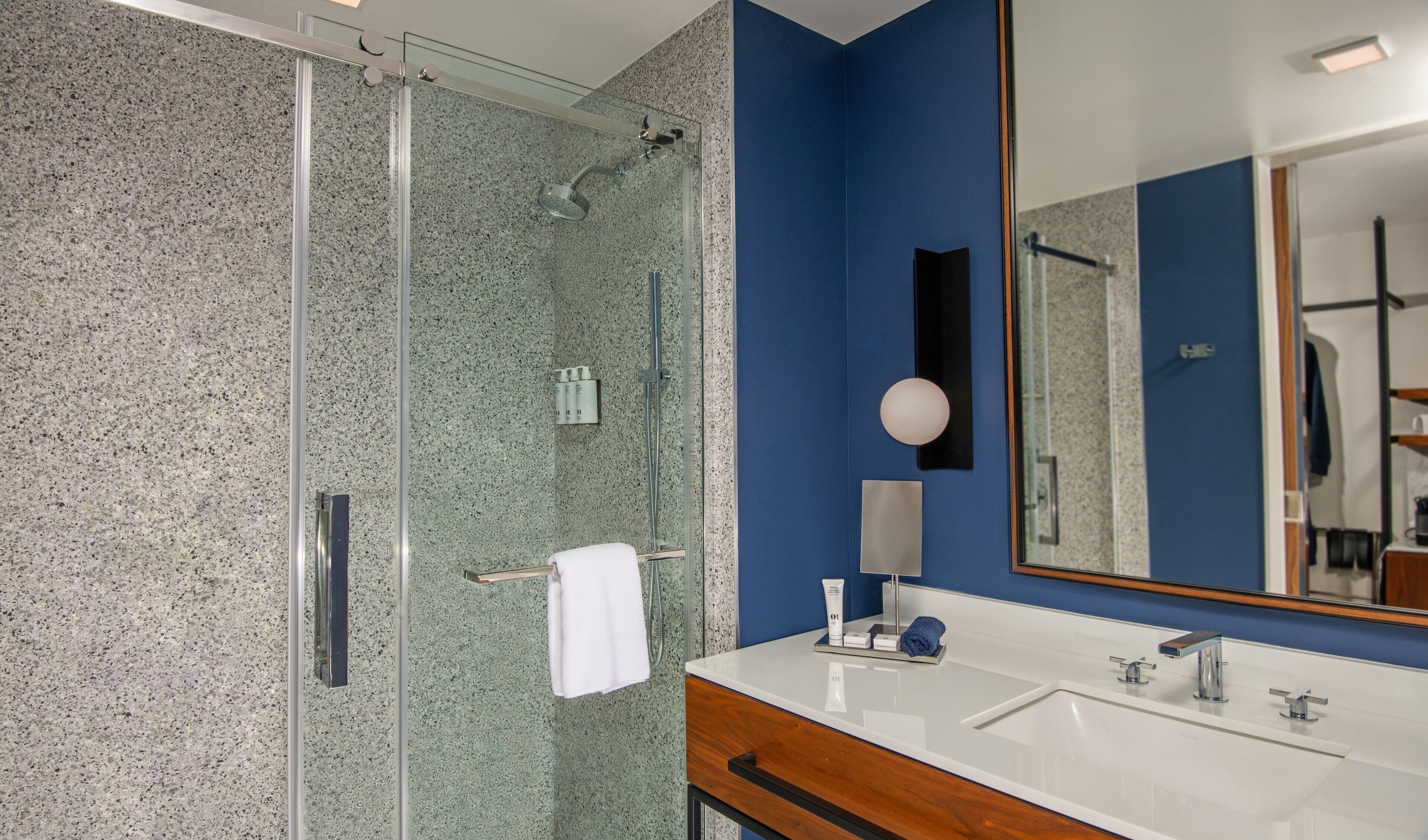 Une salle de bain moderne avec une douche à parois de verre, un grand miroir et un meuble-lavabo blanc doté d’une armoire en bois.