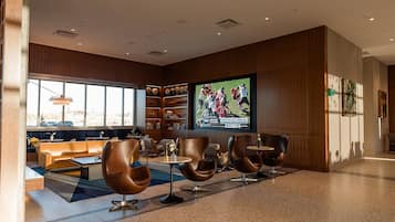 A modern lounge area with leather sofas, a large flat-screen TV, and a bookshelf with decorative items.