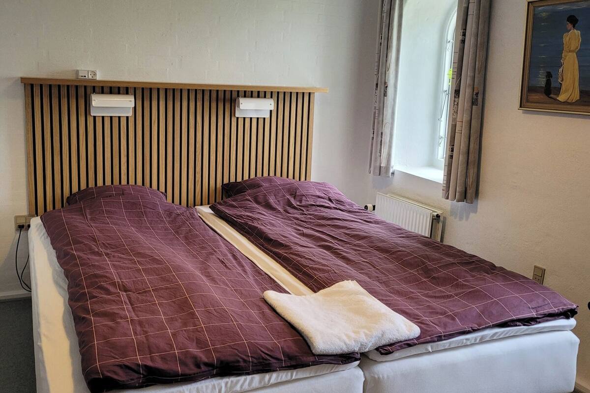 Ein Doppelbett mit Holz Kopfteil, ein Nachttisch, ein Fenster mit Vorhängen und ein Gemälde an der Wand.