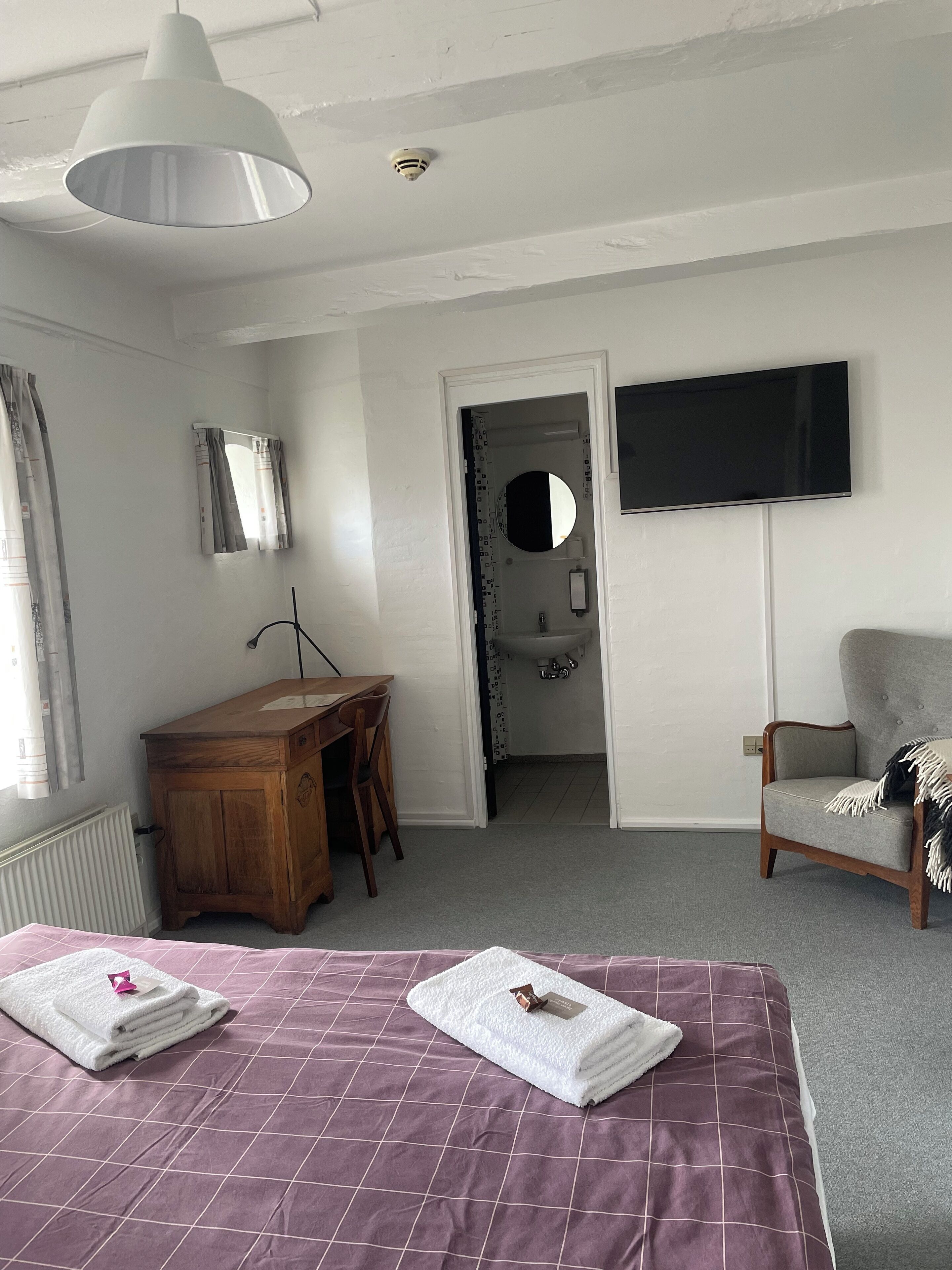 Een slaapkamer met een bed, een bureau, een stoel, een televisie en een badkamer zichtbaar door een geopende deur.