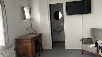 Een slaapkamer met een bed, een bureau, een stoel, een televisie en een badkamer zichtbaar door een geopende deur.