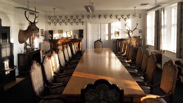 Een chique eetzaal met een lange houten tafel en versierde stoelen, omringd door aan de wand opgehangen dierenkoppen.