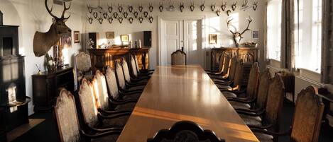 Un comedor formal con una larga mesa de madera y sillas ornamentadas, rodeado de trofeos de animales en las paredes.