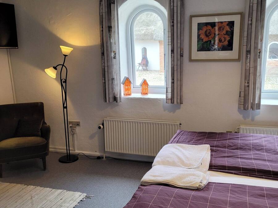 A hotel room with two beds, a sofa, a floor lamp, and a radiator.