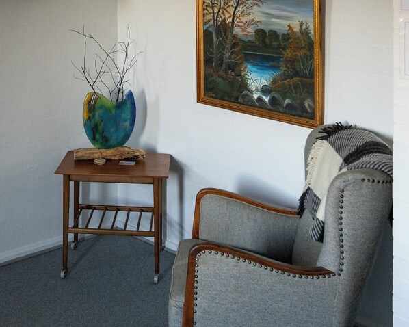 A room with a wooden side table holding a vase and a framed painting on the wall.