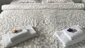 Un lit double avec une couvre-lit à motifs de feuilles, deux oreillers et deux serviettes pliées posées sur le lit.
