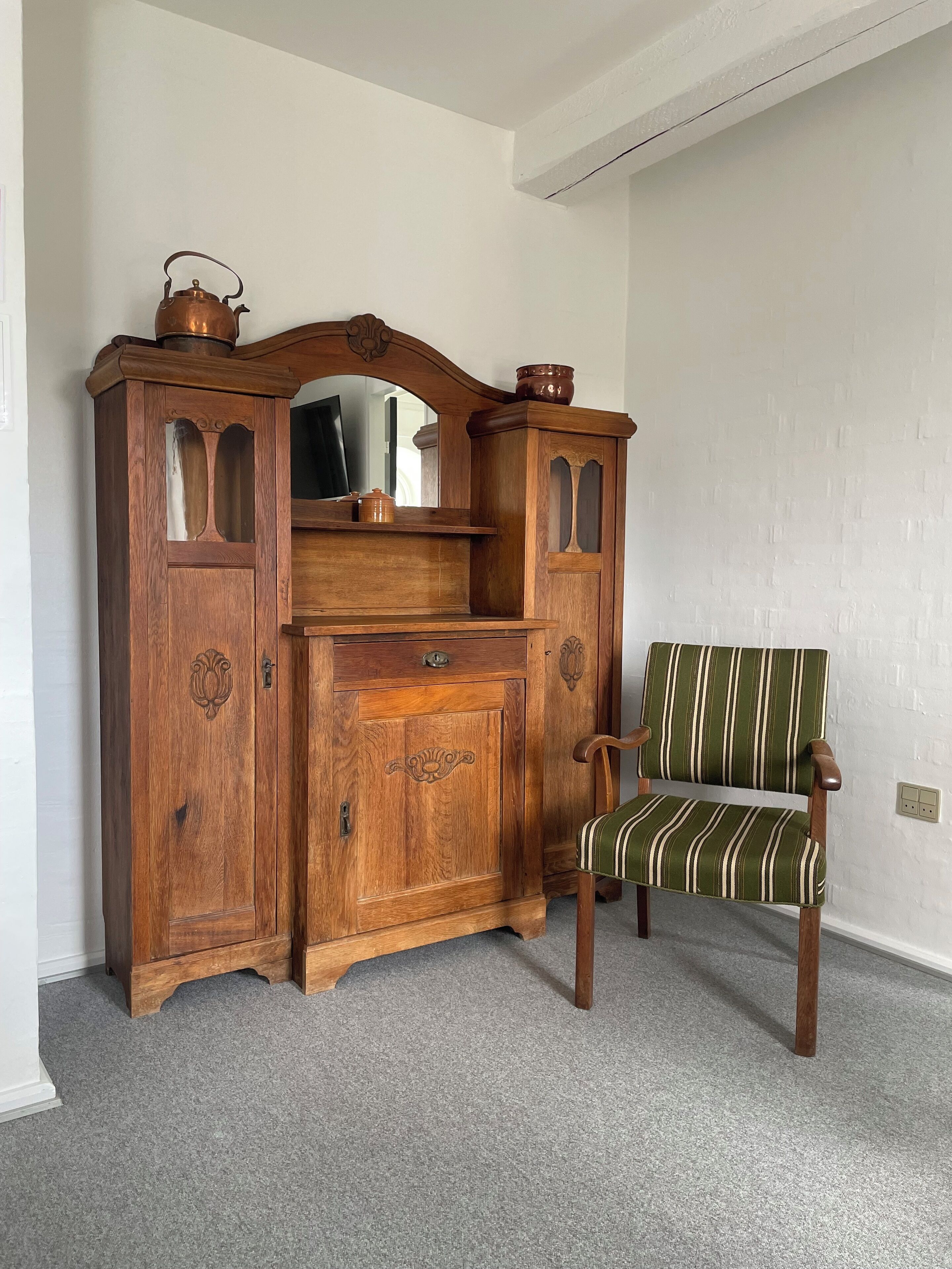 Een houten dressoir met spiegel en een stoel met gestreepte bekleding.