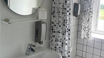 Een badkamer met een wit wastafelmeubel, een spiegel, een douchegordijn met een geometrisch patroon en een raam met uitzicht op groen.