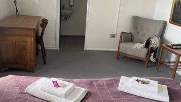 Habitación de hotel con cama, escritorio de madera, silla, televisor y baño visible a través de una puerta abierta.