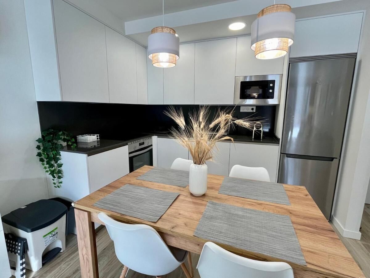 Une cuisine moderne avec des meubles blancs, des appareils en acier inoxydable et une table à manger en bois agrémentée de sets de table.