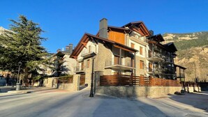 Un immeuble à plusieurs étages, doté de balcons et d’une façade en pierre, avec une chaîne de montagnes en arrière-plan.