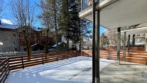 Un espace extérieur enneigé avec un bâtiment en pierre, des bancs en bois et une rambarde en métal.