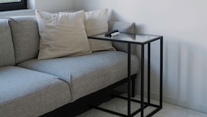 Une pièce moderne avec un canapé gris, une petite table noire et une fenêtre équipée de stores.