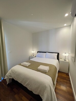 A neatly made bed with white linens and a brown throw blanket, two bedside lamps, and a small nightstand. - Aldoar House - Cozy house near City Park and Beach (Porto)