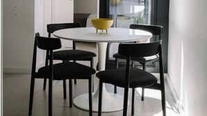 Un espace repas moderne avec une table ronde blanche, des chaises noires et un bol jaune.