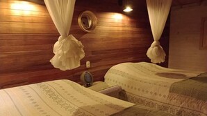 Una habitación con dos camas, cada una con ropa de cama estampada, una mesita de noche con un florero y un espejo montado en la pared.