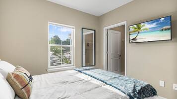 A bedroom with a bed, a window, a door, and a wall-mounted TV.