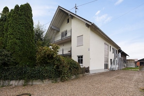 A two-story building with a balcony, a staircase, and a gravel driveway. - Apartment 'Ferienwohnung Griaß Di' with Balcony and Wi-Fi (Salgen)