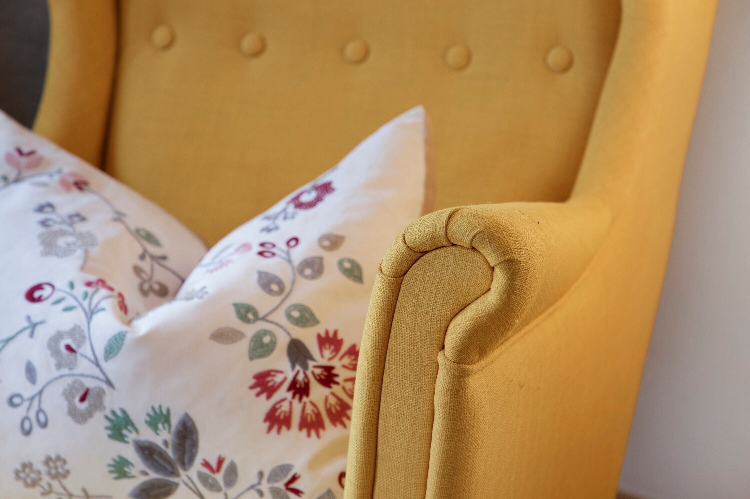 Un sillón tapizado de color amarillo con un cojín estampado con flores.