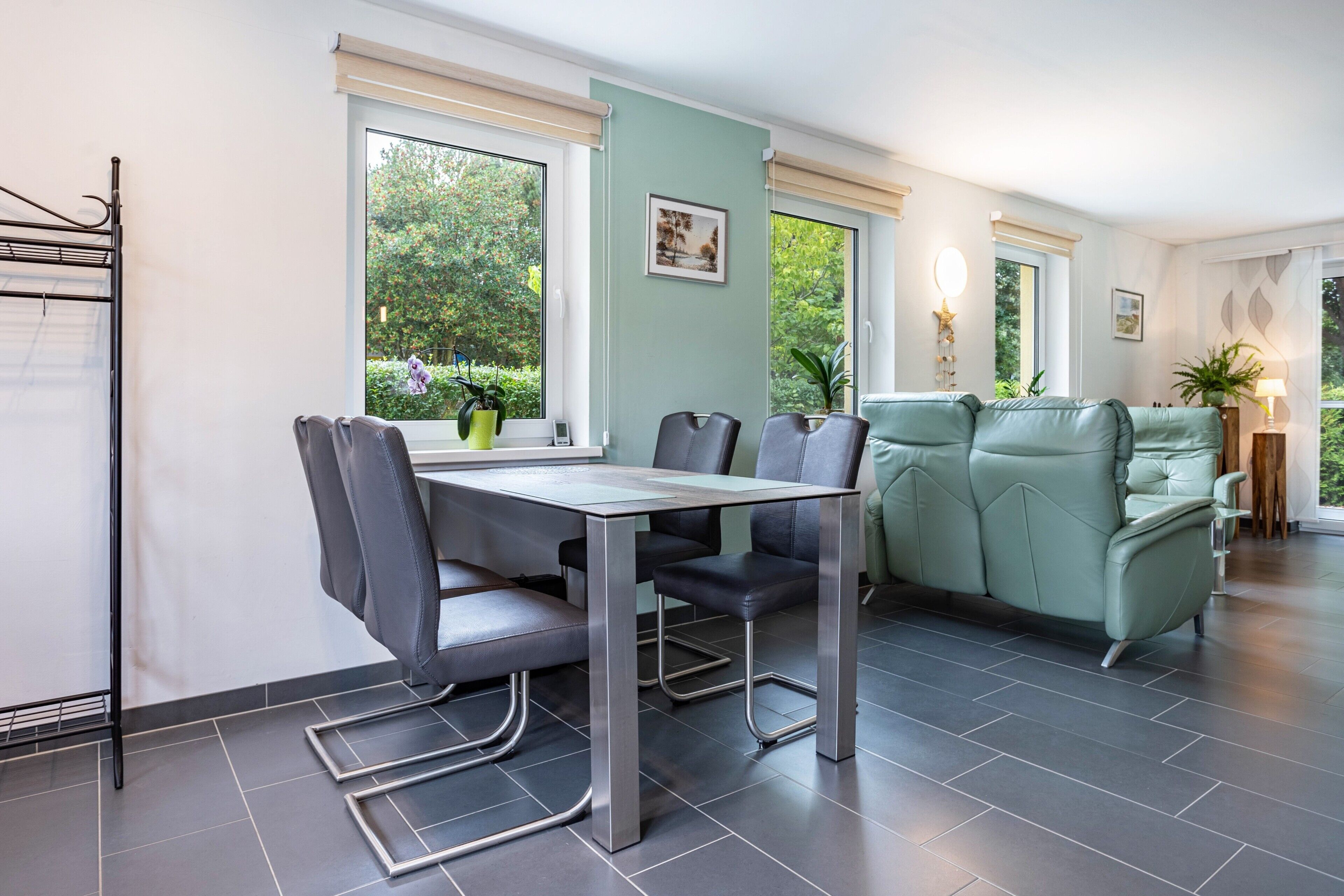 A modern living room with a dining area, large windows, and a green sofa.