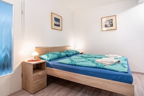 Un lit bien fait, avec une literie bleue, une table de chevet en bois sur laquelle se trouve une lampe, et deux tableaux encadrés accrochés au mur.