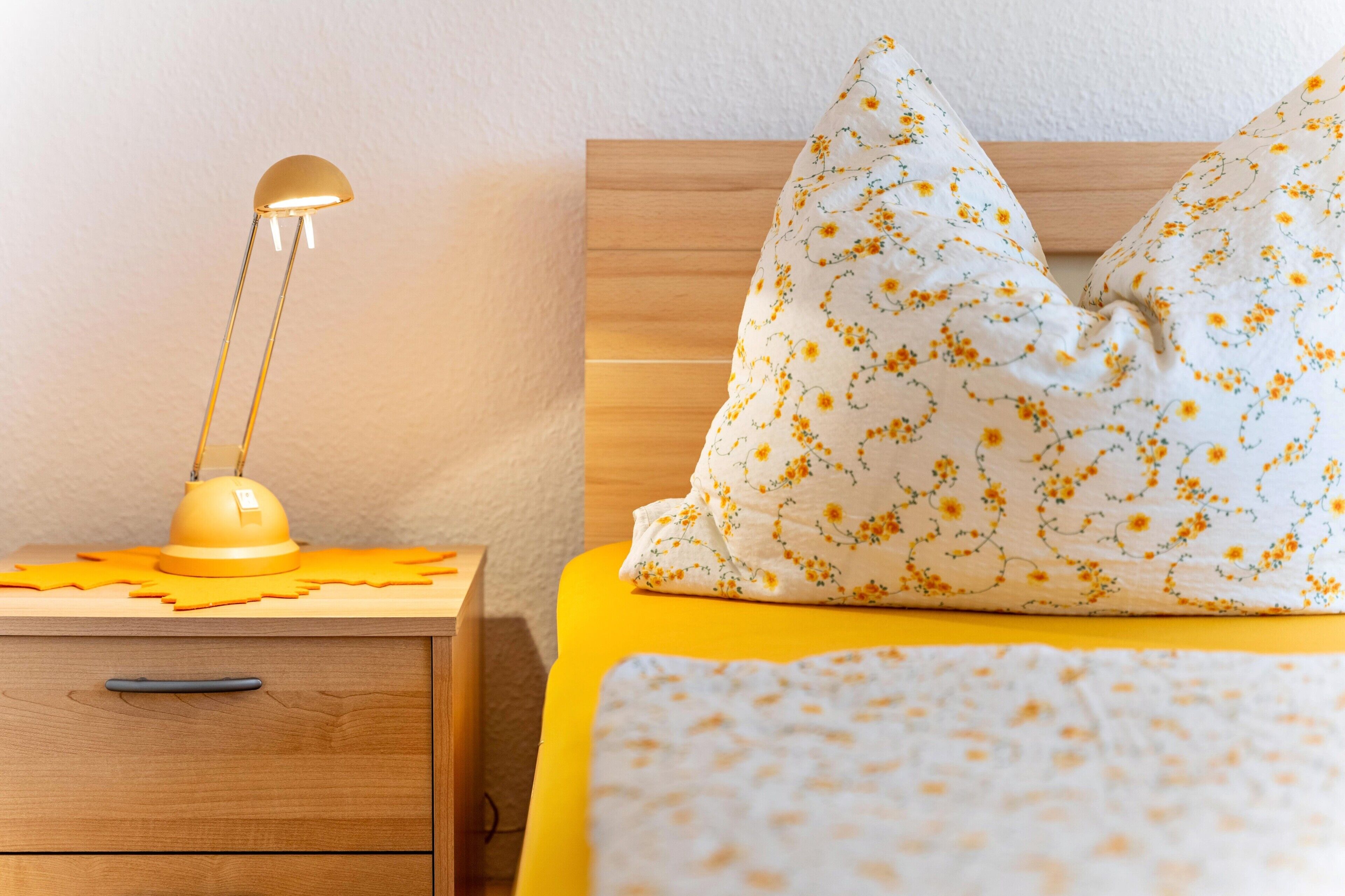A bed with a floral-patterned pillow, a bedside lamp, and a wooden nightstand with drawers.