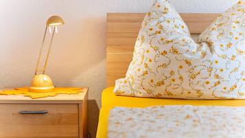 A bed with a floral-patterned pillow, a bedside lamp, and a wooden nightstand with drawers.