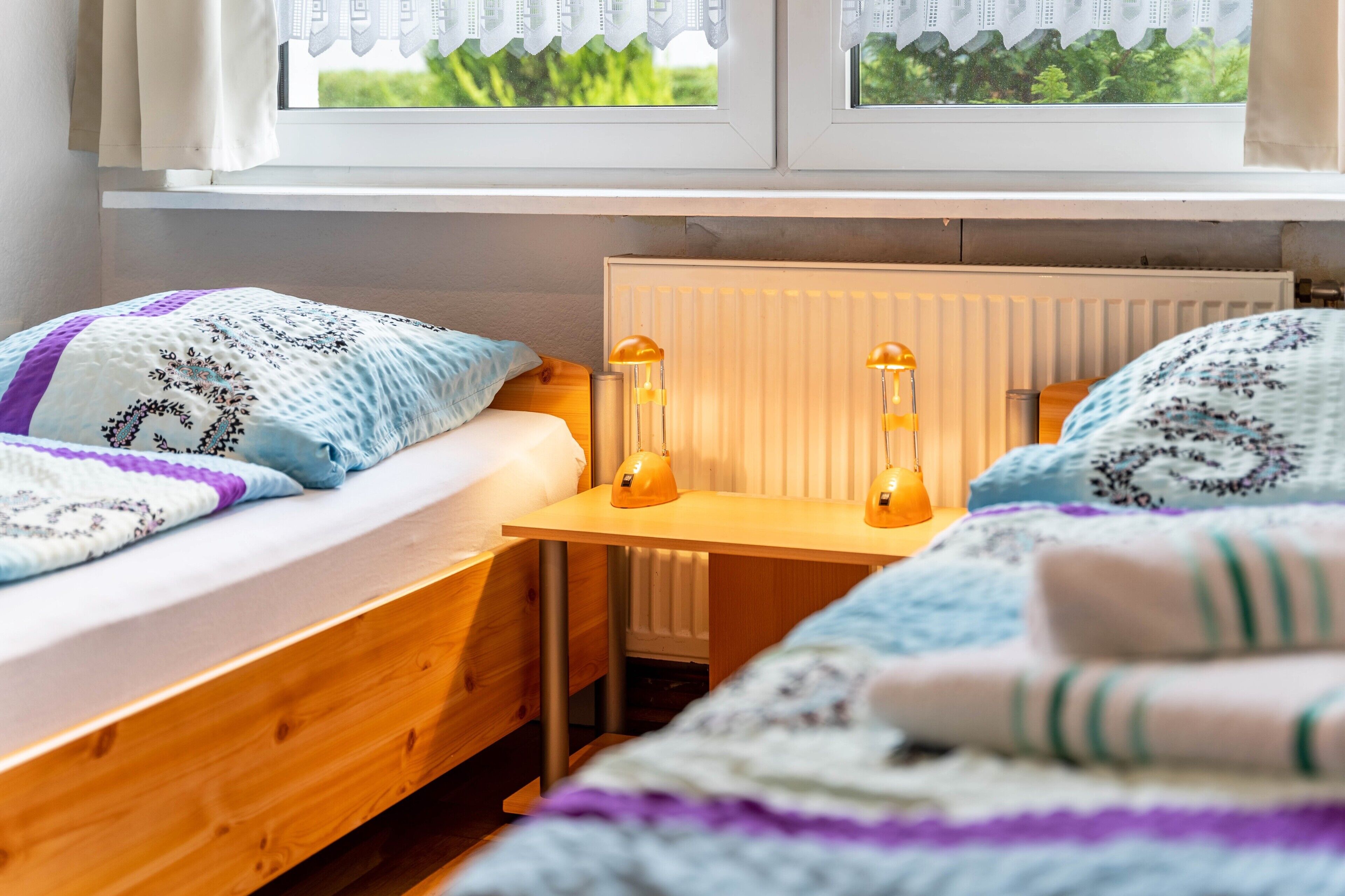 A bedroom with two single beds, a wooden desk, two wall-mounted lamps, and a radiator.