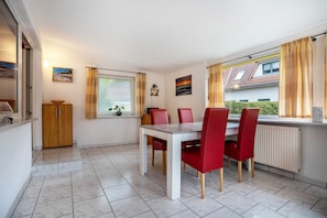A dining area with a table and chairs, a window with curtains, a radiator, and a cabinet.