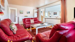 A living room with red leather sofas, a glass-top coffee table, and a large mirror reflecting the room. - Apartment 'Prerow Am Deich - Fewo 3' with Private Terrace, Private Garden and Wi-Fi (Prerow)