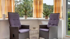 Two wicker chairs with cushions, a small round table, and potted plants on a balcony with a view of trees. - Apartment 'Prerow Am Deich - Fewo 3' with Private Terrace, Private Garden and Wi-Fi (Prerow)