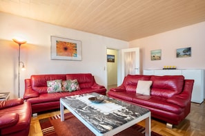 A living room with two red leather sofas, a marble coffee table, a floor lamp, and a painting on the wall.