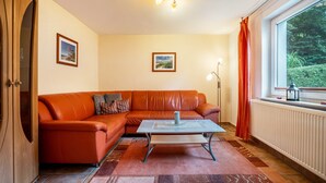 A living room with a leather sofa, a coffee table, a floor lamp, and a window with curtains. - Apartment 'Prerow Am Deich - 4' with Private Terrace, Private Garden and Wi-Fi (Ostseebad Prerow)