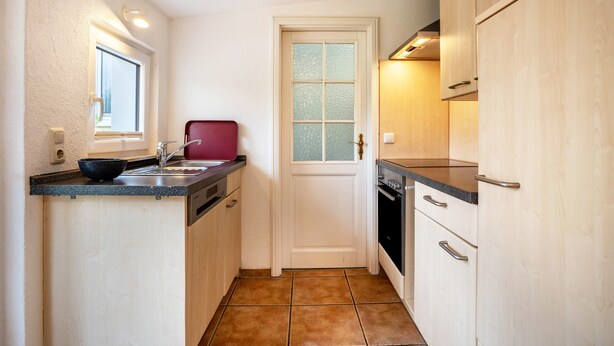 A compact kitchen with a window, a door with frosted glass, and a built-in oven. - Apartment 'Prerow Am Deich - 4' with Private Terrace, Private Garden and Wi-Fi (Ostseebad Prerow)