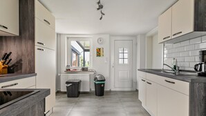Una cocina moderna con armarios de colores claros, un cubo de basura negro, una puerta blanca y una ventana con vistas.