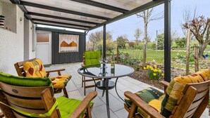 Un patio al aire libre con una mesa y sillas redondas, un área techada y vistas al jardín.